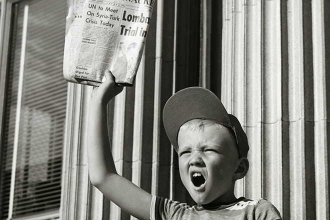 Boy selling newspapers in front of a building